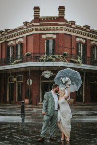 GLOOMY BRIDE AND GROOM PORTRAIT IN NEW ORLEANS KISSING UNDER CLEAR UMBRELLA IN THE RAIN
